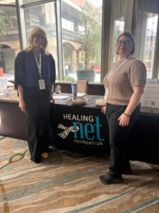 Board Member Stephanie Alband and Executive Director Ashlee Russeau-Pletcher stand in front of a table with the Healing NET Foundation Logo
